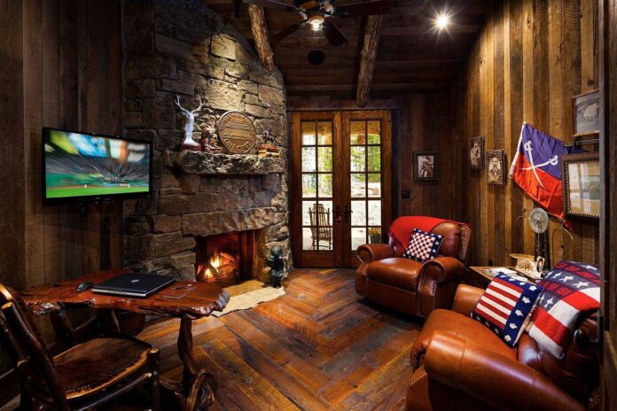 Gorgeous mountain cabin-inspired small rustic home office with stone walls. fireplace, live-edge desk and comfy seating
