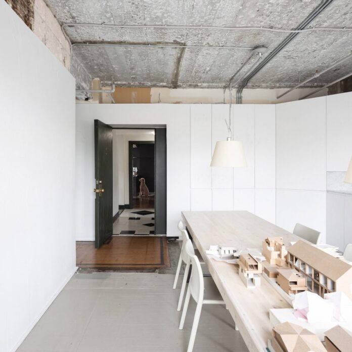 Meeting room with long wooden table, exposed concrete ceiling and tiled entrance in D'Arcy Jones Architects' self-designed studio in Vancouver