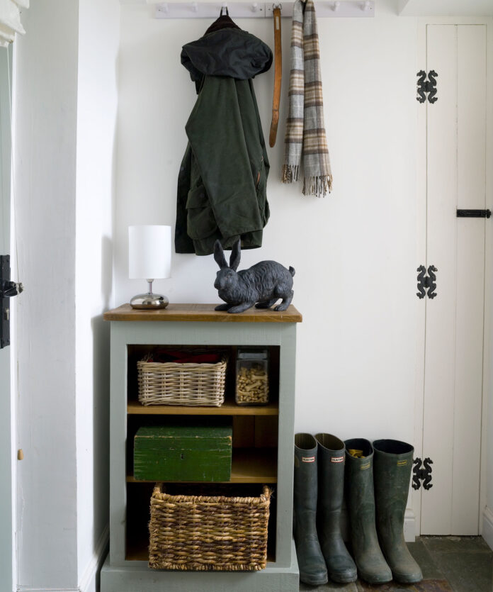 White hallway with coats hung high and boots propped by the door