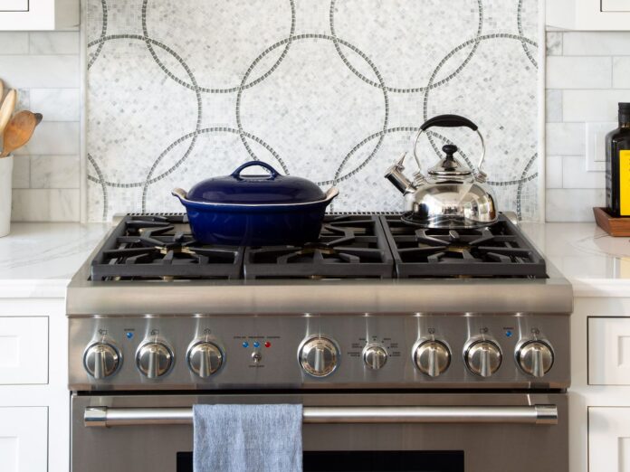 A clean stainless steel gas stove with white cabinets.