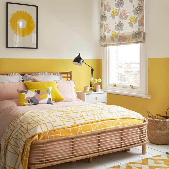 Yellow bedroom with two tone wall, floral blind, black task lamp, cane bed frame and yellow geometric rug