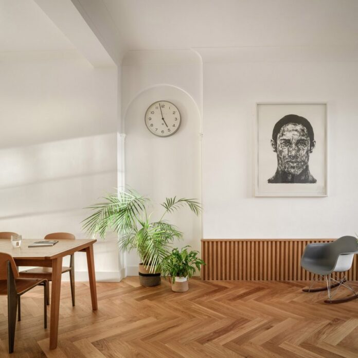 Lounge with wooden dining table and grey rocking chair in front of portrait illustration in 19th-century Leith apartment designed by Luke McClelland