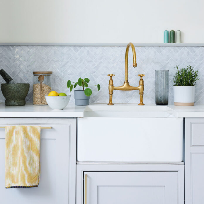 Butlers sink set into pale grey kitchen units with grey tiled splash back and copper mixer tap.