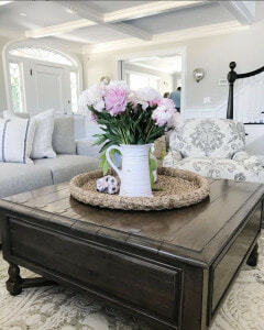 Square dark stained coffee table with a vase of peonies.