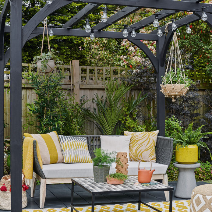 Patio with outdoor rug and furniture underneath black pergola with festoon lights