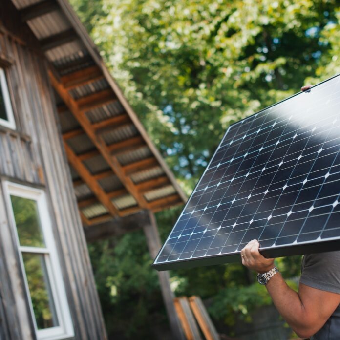 A man carrying a solar panel on a green construction site, working on a green building project.