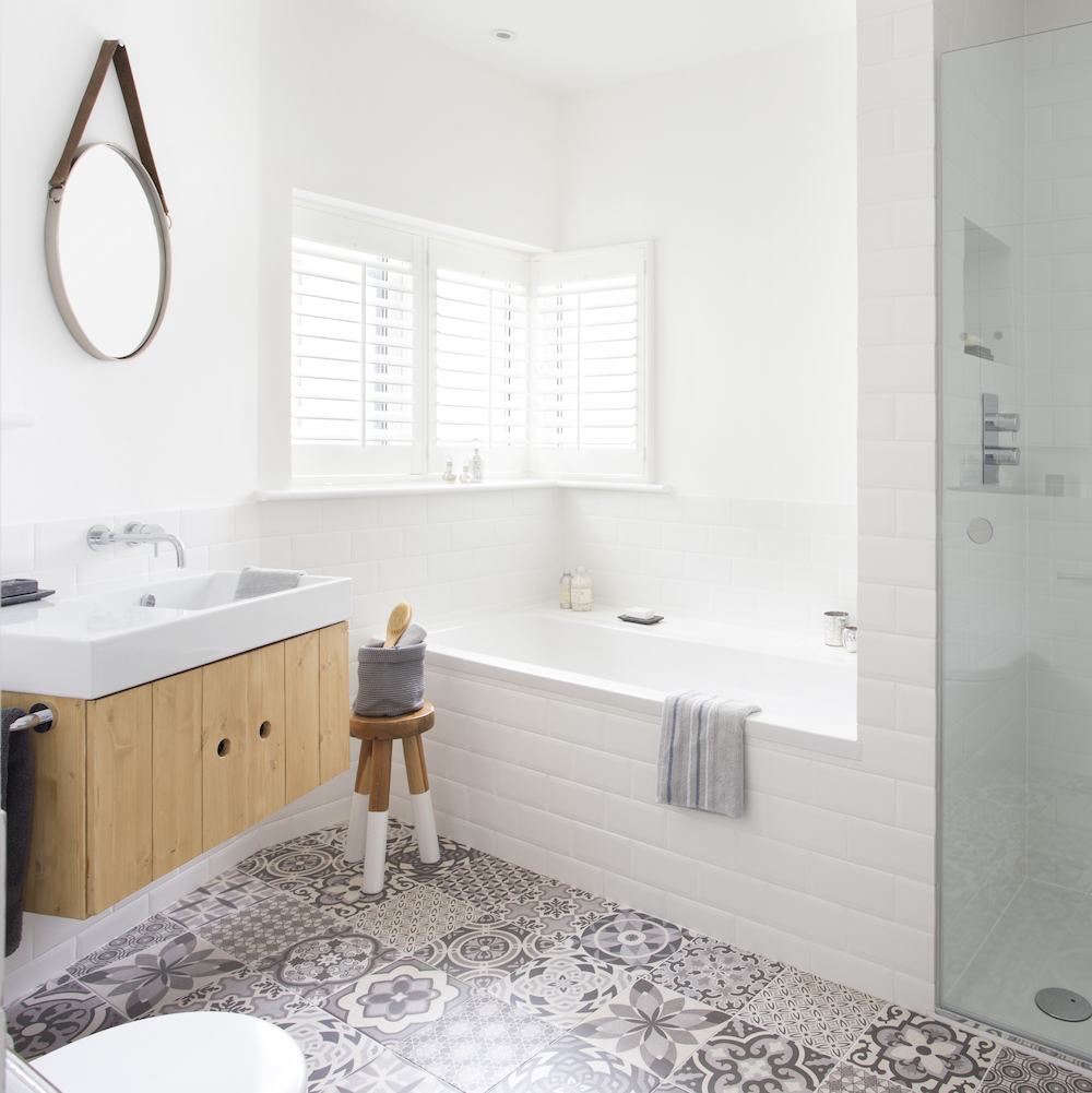 White bathroom with white tiled bath surround and grey patterned tiled floor