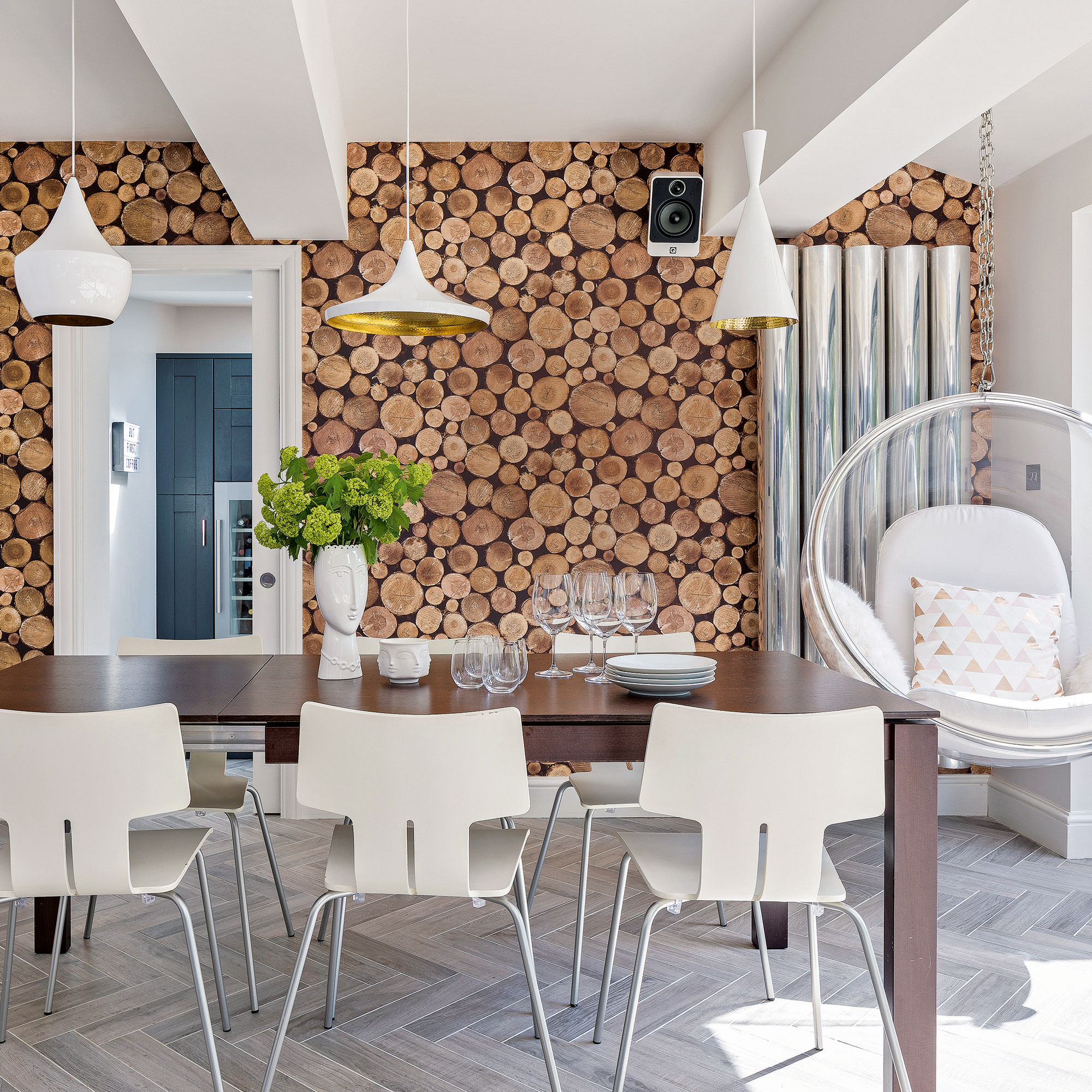 dining room with timber table and white chairs wood wallpaper white pendant lights perspex egg hanging chair speakers