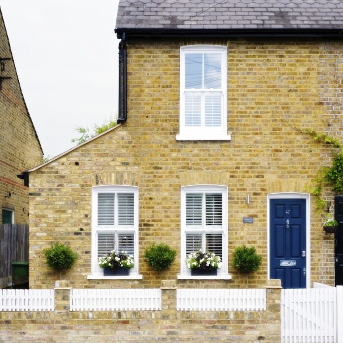 Exterior of end of terrace brick house with blue door and white fence.