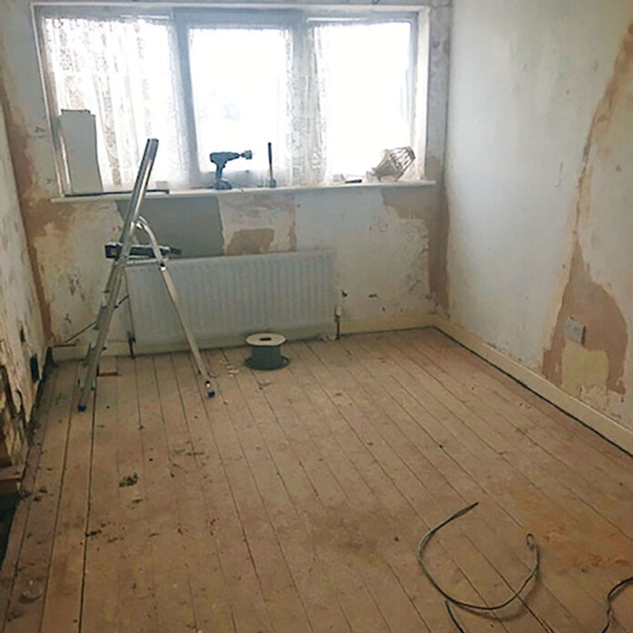 Empty renovated room with bare floorboards, stripped walls, step ladder and cables