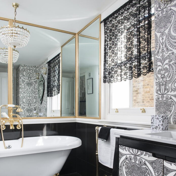 Glamourous bathroom with mirrored wall, gold details, rolltop bath and chandelier