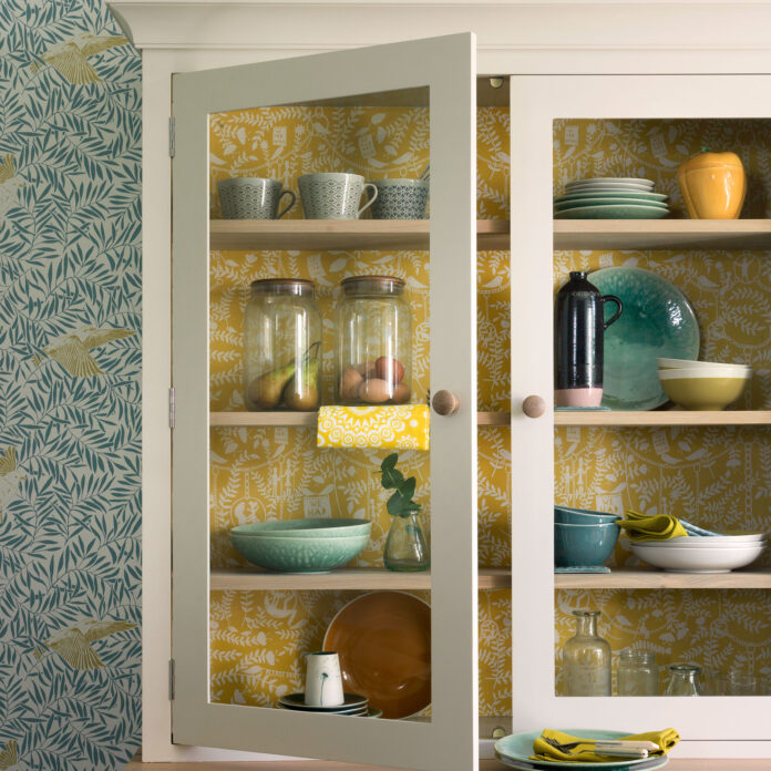 Close up of cream dresser with yellow patterned wallpapered interior and blue wallpaper on wall