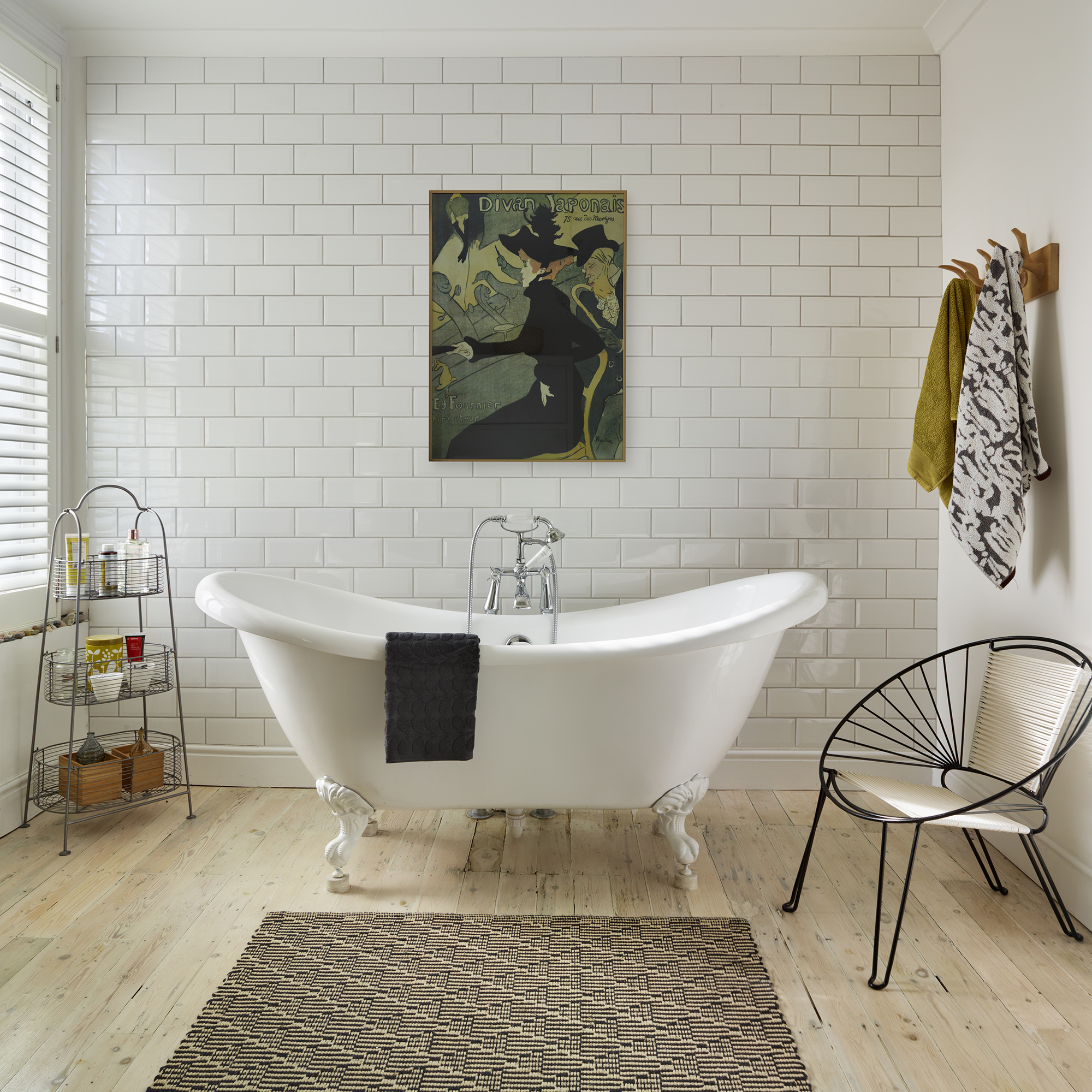White metro tile bathroom, framed artwork, patterned rug, freestanding rolltop bath, soap shelf rack