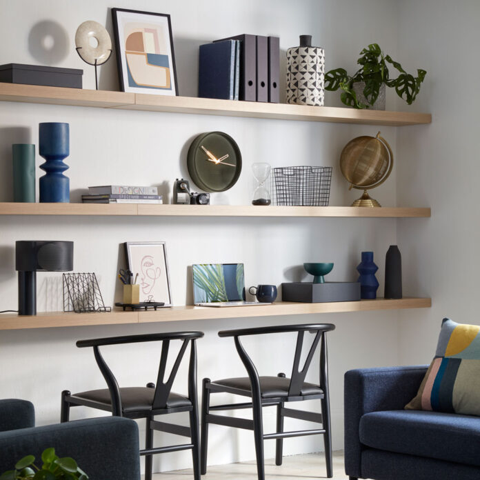 A living room office with wooden shelves and two black wishbone chairs