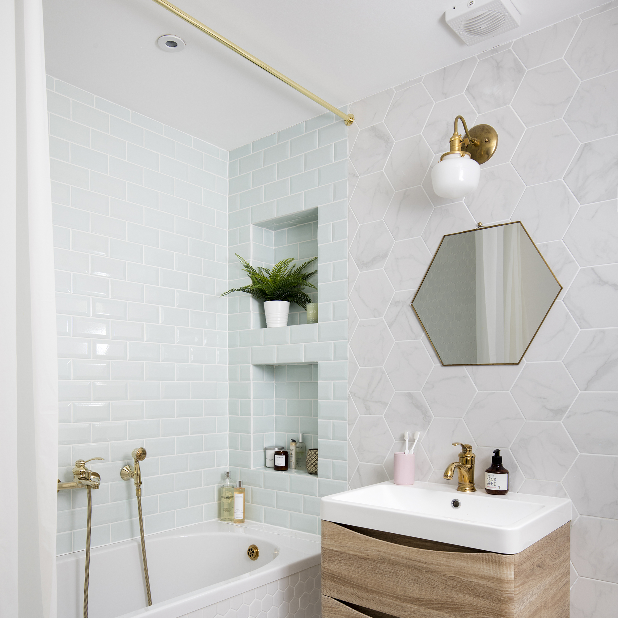 Bathroom with white wall and floor tiles, bathtub and golden mirror over wooden vanity unit.