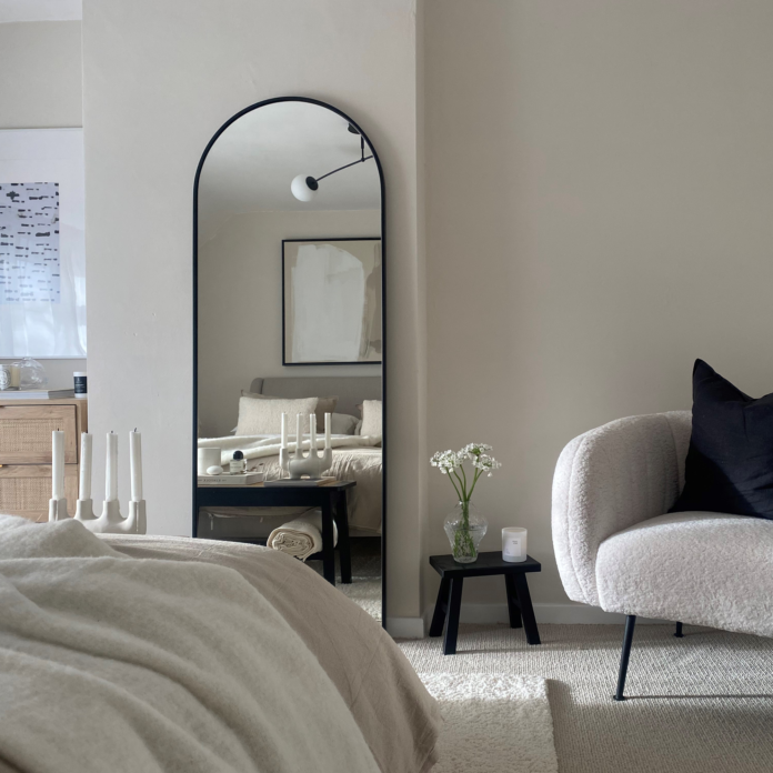 neutral bedroom with boucle armchair and arched mirror