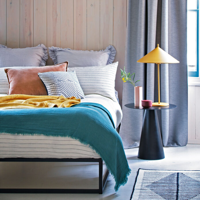 Bedroom with dressed bed, black side table and grey curtains