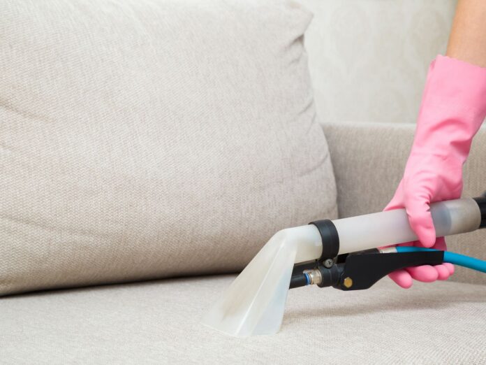 A pink gloved hand cleaning couch upholstery. 