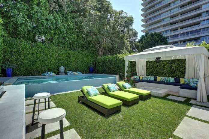 Modern above ground pool featuring a Buddha statue beside wicker sun loungers with lime green cushions. A cabana adds to the backyard design with a concrete sectional and fire pit.