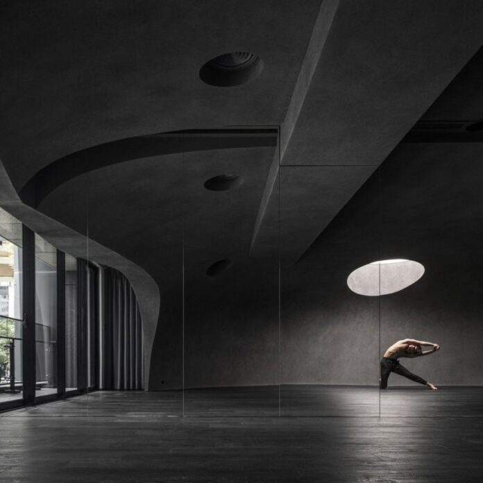 Person doing yoga in dark studio space beneath round skylight
