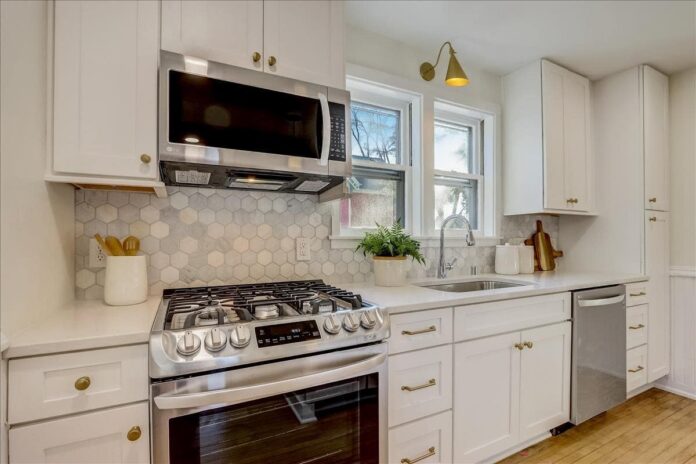 One wall shaker white kitchen cabinets in Victorian home with gold accents and marble backsplash