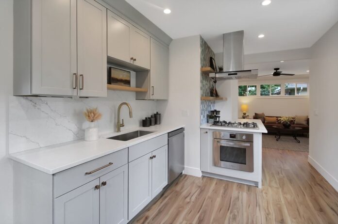 Light gray, one-wall shaker kitchen cabinets with brass hardware, and marble slab backsplash