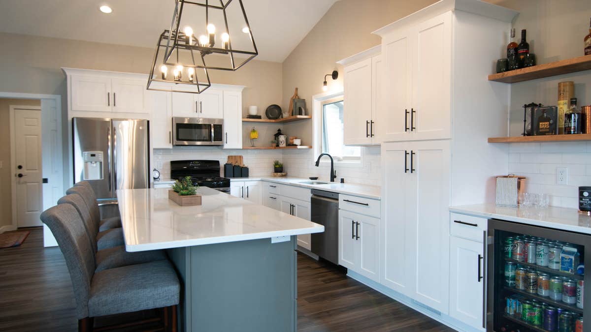 White shaker kitchen cabinets with a gray island, white quartz countertops and bronze accents