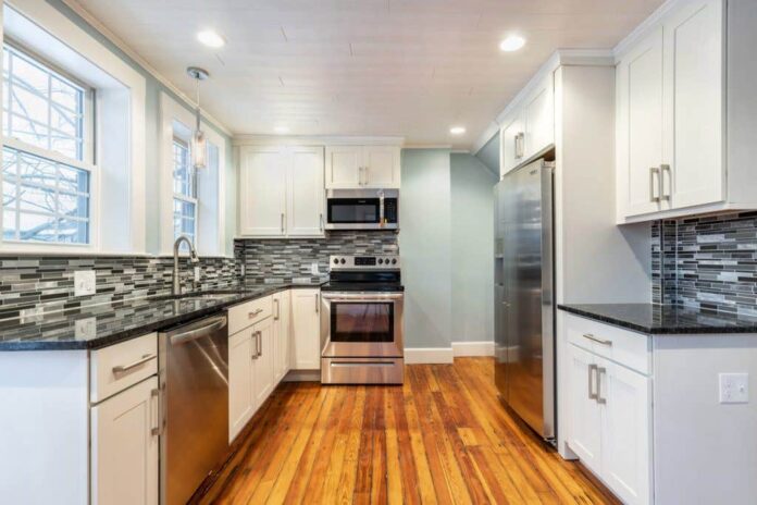 small u-shaped kitchen with white cabinets, light blue walls, black countertops and original wood floors