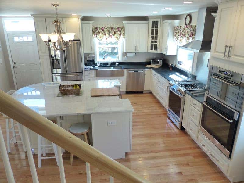 kitchen viewed from staircase has wide plank white oak flooring, painted white traditional cabinets, built-in ovens, glass mullion door cabinet, black granite countertops and large island with white granite counter.