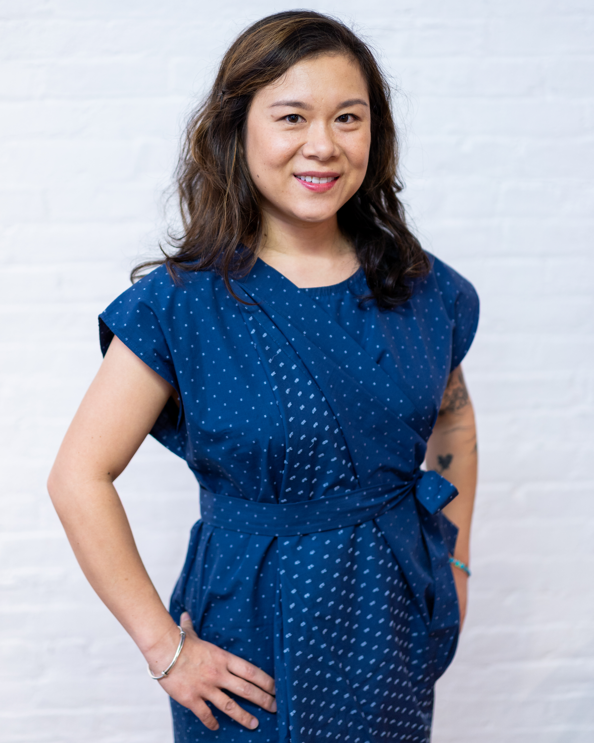 Image of an Asian-American woman in a navy blue dress standing in front of a white brick wall