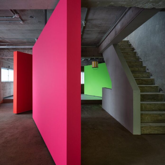 Pink, orange and green rotating partition walls in a concrete apartment by AB Rogers