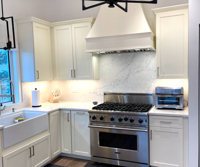 Cream-colored shaker kitchen cabinets with a matching wood hood and large stainless steel gas range