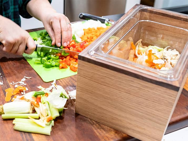 Person chopping up vegetables and adding scraps to compost bin.