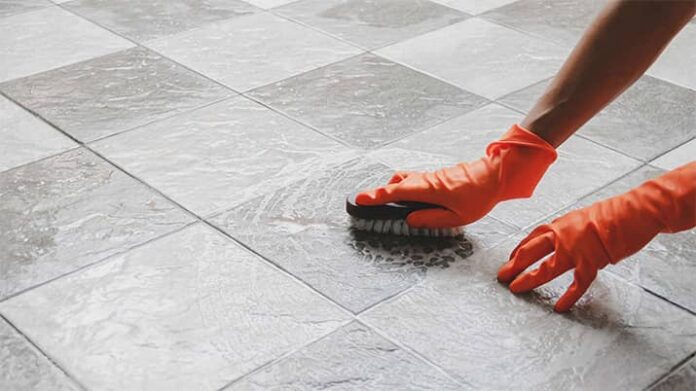 Individual wearing gloves cleaning flooring grout.