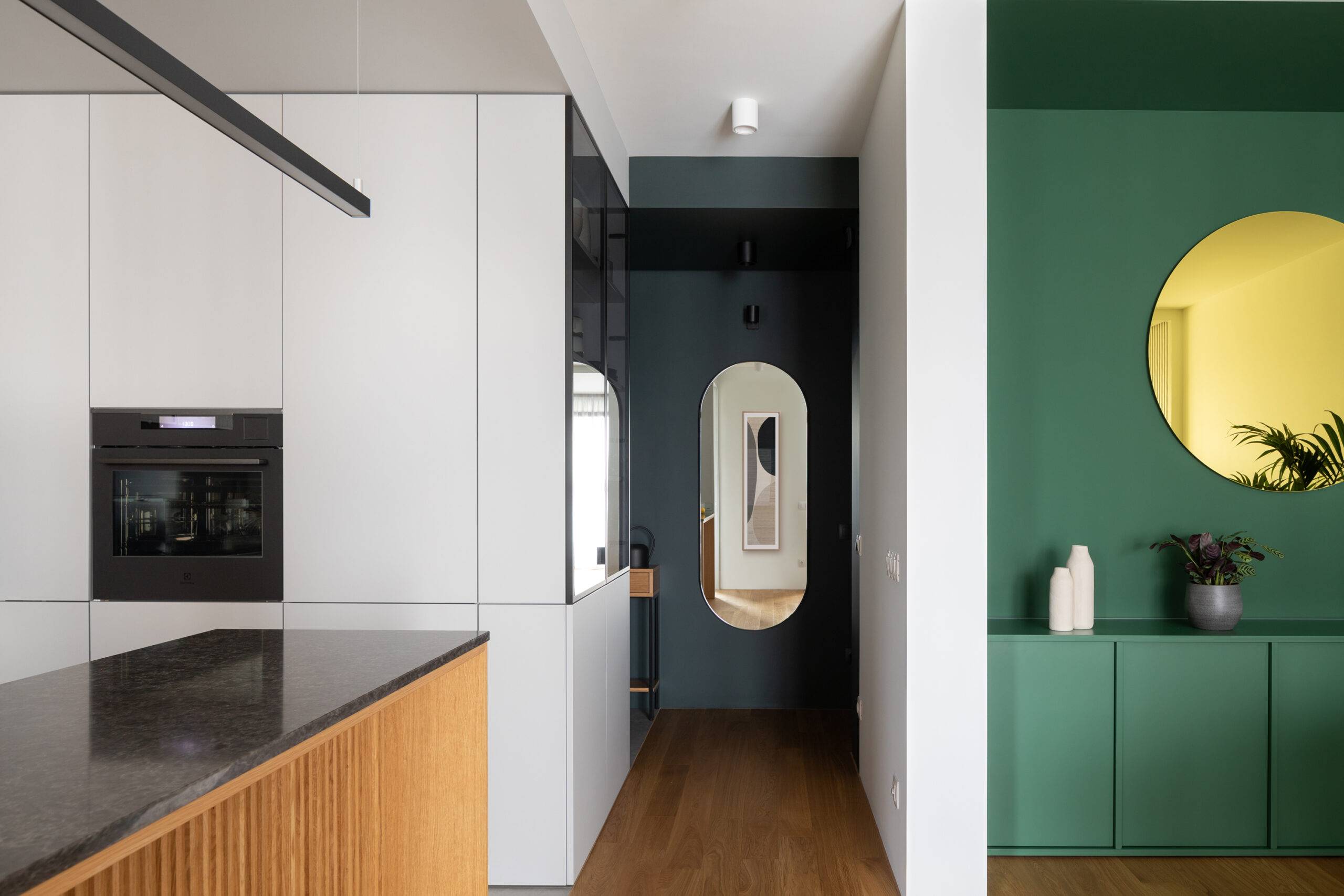 hallway with oval mirror at the end, green accent wall to the right and white kitchen to the left