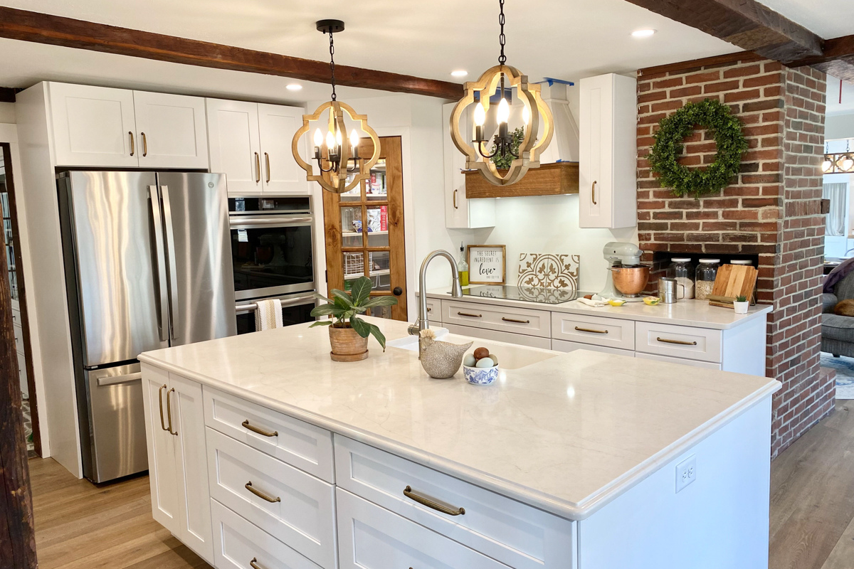 White shaker farmhouse kitchen with rustic wood beams, a large island, white quartz countertops and a large matching kitchen hood.