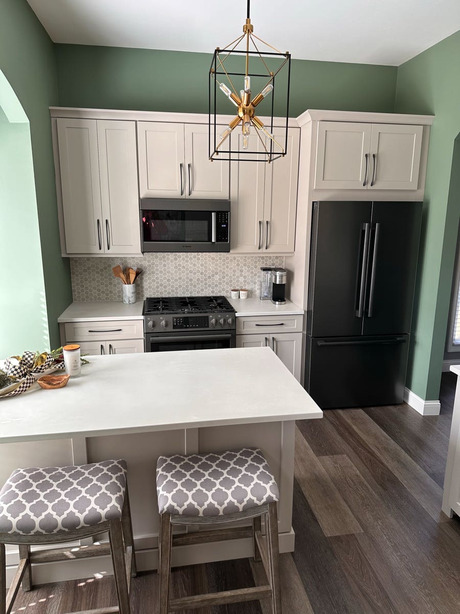 Light gray shaker kitchen cabinets with a small, decorative island with a built-in bookcase, green walls, and a neutral tile backsplash