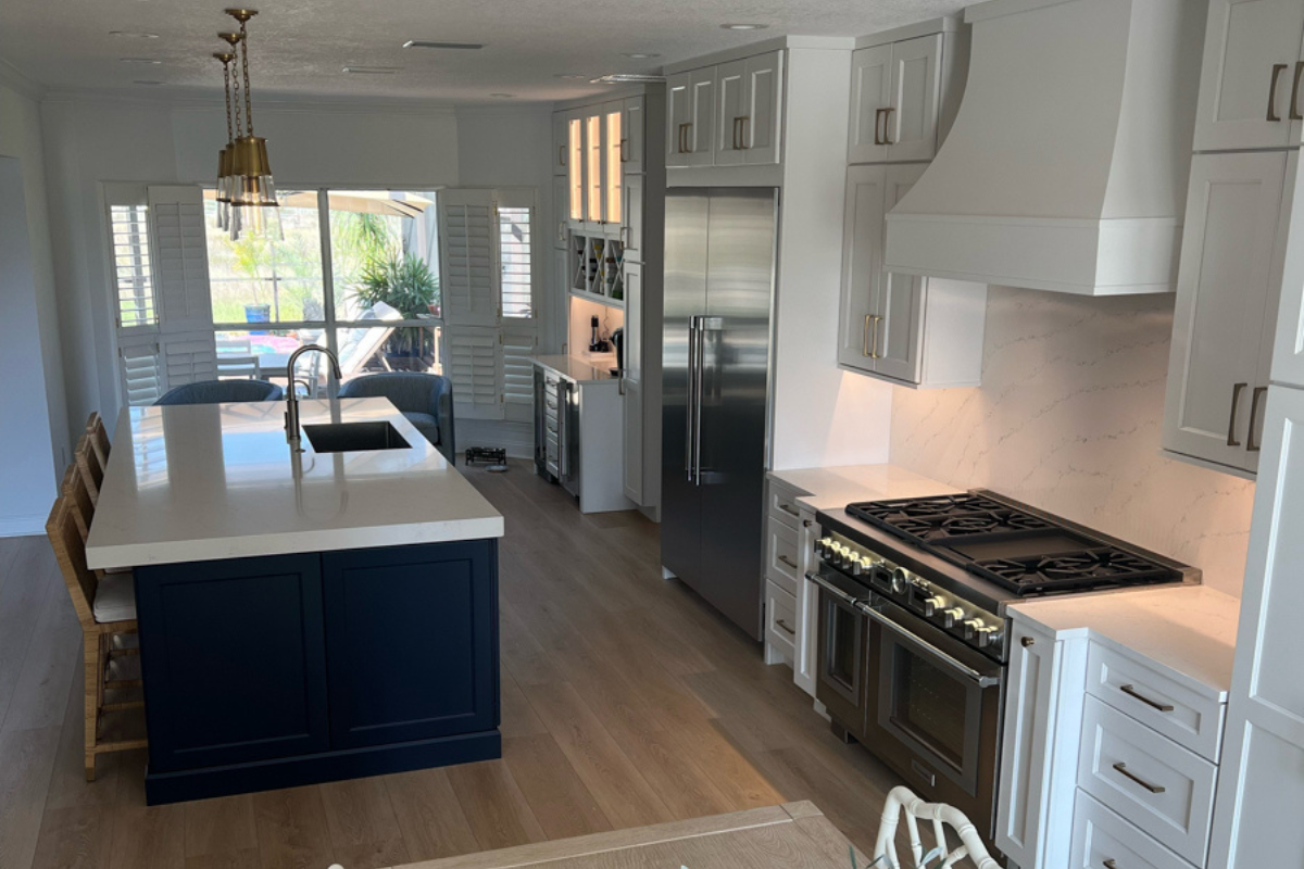 Grand decorative white shaker kitchen design with stacked cabinets, an artisan kitchen hood, navy blue island cabinets, and white quartz countertops