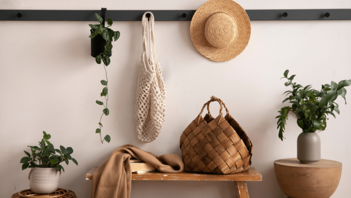 composition of cosy entryway with wooden bench, coffee table, basket, hanger and personal accessories. Beige wall.