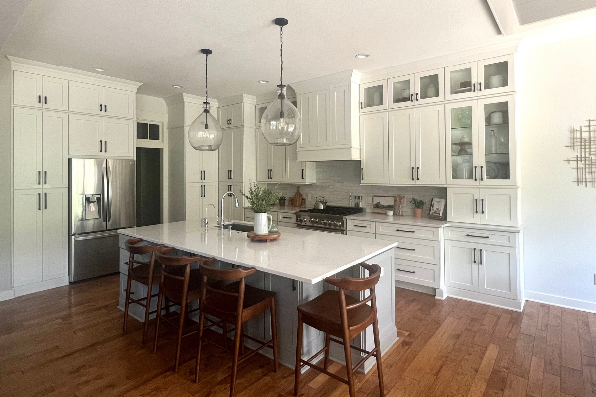 Stacked white shaker kitchen cabinets with glass and crown molding, a decorative wood range hood, white quartz countertops, and a medium-gray island