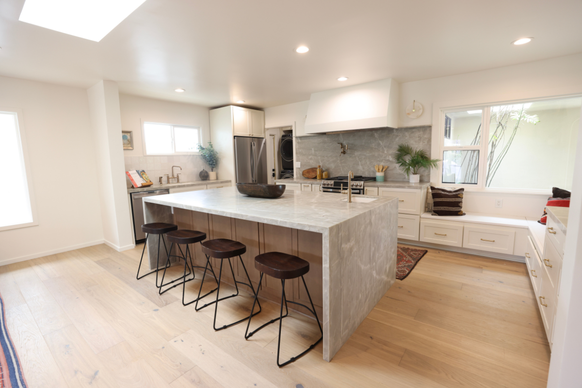 Mid-century modern cream shaker kitchen cabinet design with a large custom kitchen hood and medium wood-toned island cabinets with beautiful gray stone waterfall countertops