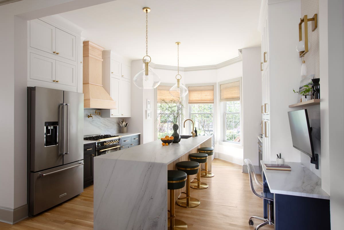 Stacked white inset shaker cabinets with black inset shaker island cabinets, creamy waterfall countertops, funky glass and gold light fixtures, and a natural wood kitchen hood
