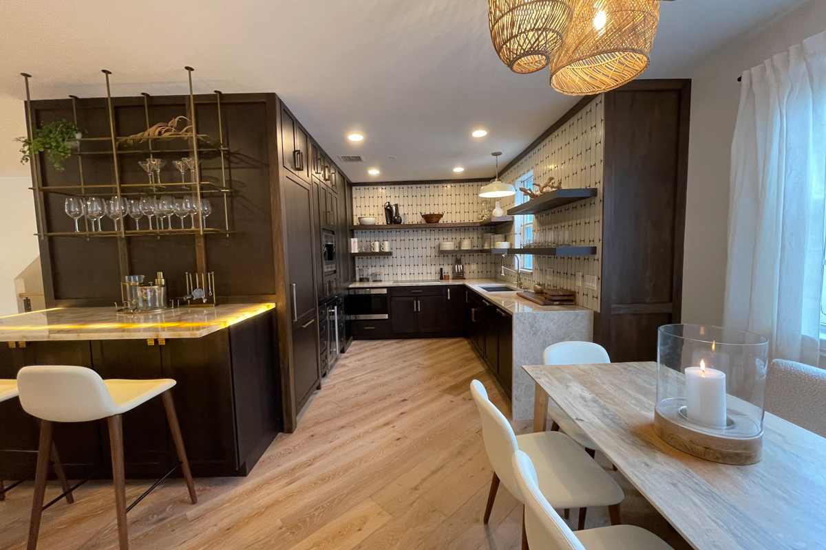 Small and chic U-shaped kitchen in dark brown shaker cabinets with wood floating shelves, white funky tile backsplash, and light brown quartz countertop with waterfall edge detail