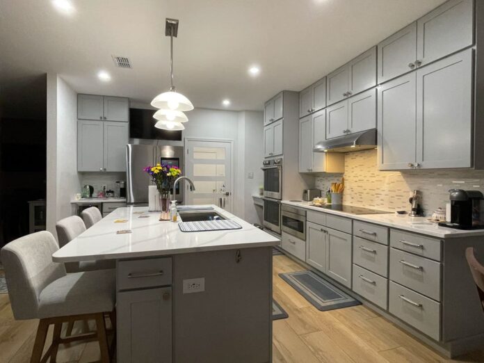 Light gray stacked shaker kitchen cabinets and island with white quartz countertops, brushed nickel cabinet hardware and modern pendant lighting