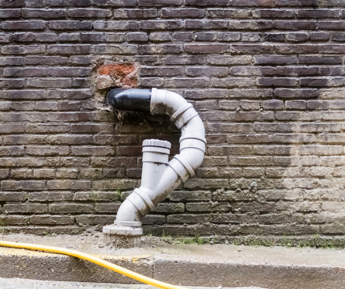 A toilet bowl with a drain line and a vertical pipe leading to the roof