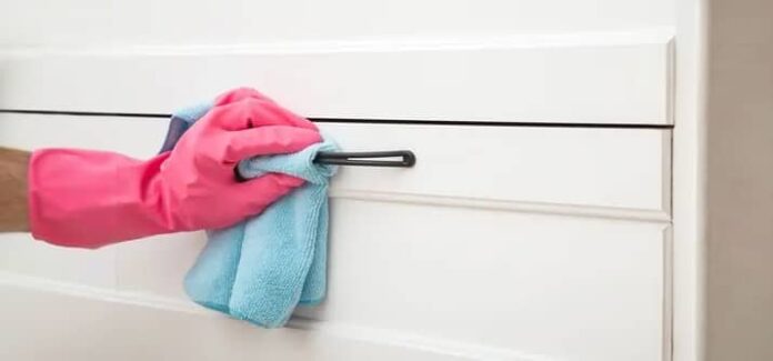 Person wearing pink glove cleaning kitchen cabinet with cloth.