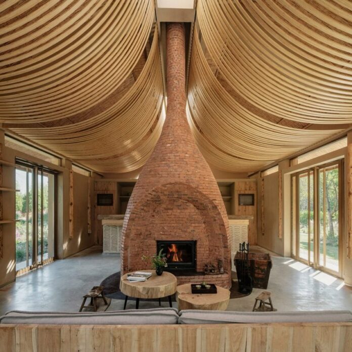 Strips of wood curve from the ceiling, while a central brick fireplace divides the open space