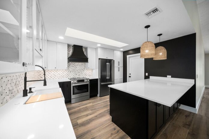 Bright kitchen with white wall cabinets with glass inserts and black base cabinets with white quartz countertops