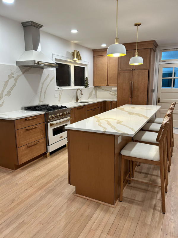 Warm medium-brown shaker kitchen design with a large island with white quartz and minimal design.