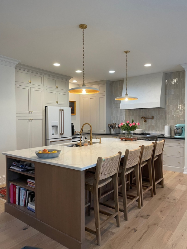 Cream colored inset shaker kitchen cabinets with warm wood-toned island, tan quartz countertops and textured glazed tile backsplash behind a tapered kitchen hood